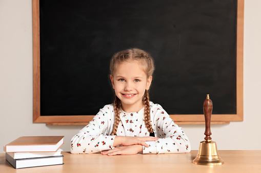 Pupil sitting at desk with school bell and books in classroom