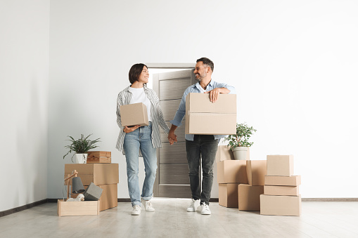 Happy couple with moving boxes entering in new apartment