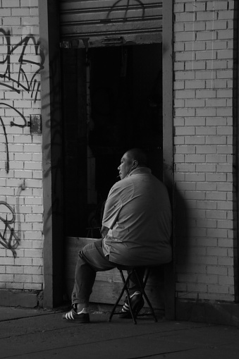 NYC, United States – April 16, 2023: A grayscale shot of a man sitting in a chair in front of a wall featuring a vibrant graffiti mural.