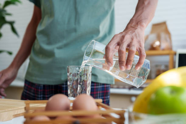 istock Close-up man's hands, handle pitcher, pouring clean water from pitcher into glass, in sufficient quantities drink in order drink it all in one go, after pouring, bring pitcher back its original place. 1490335365