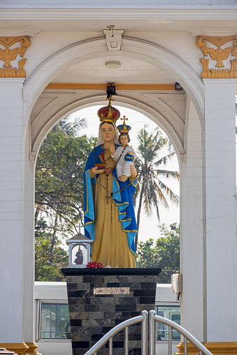 Negombo, Western Province, Sri Lanka - March 7th 2023:  Statue of Virgin Mary with Christ child in tropical surroundings outside a chapel close to the dry fish market
