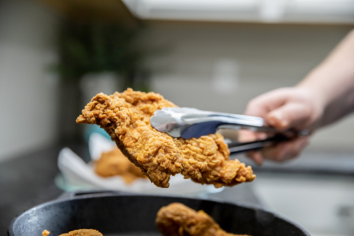 Fried chicken being prepared at home in domestic kitchen with cast iron skillet