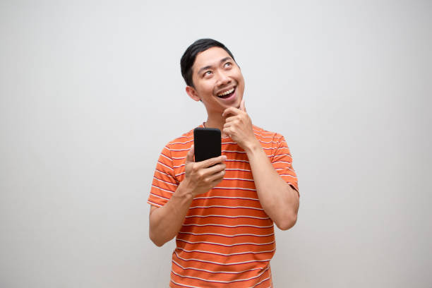 istock Asian man orange shirt holding smartphone gesture thinking looking up isolated 1490344639