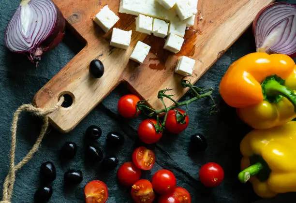 Feta cheese, black olives, tomatoes and peppers on a wooden chopping board