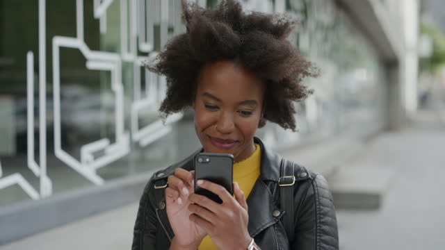 portrait of stylish african american woman using smartphone texting browsing online social media smiling enjoying reading sms messages on mobile phone technology in city street