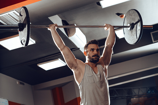 Young muscular man weight lifting a barbell at the gym.