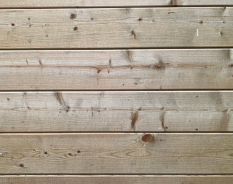 Close-up photograph of wood panelling. The slatted wooden planks contain knots. Wood grain effect. Tongue and groove pine which has been treated for exterior use. The wood is textured. Stock image of wooden panelling. Stock photograph of wood. Timber planking. Pine panelling. Pine tongue and groove.