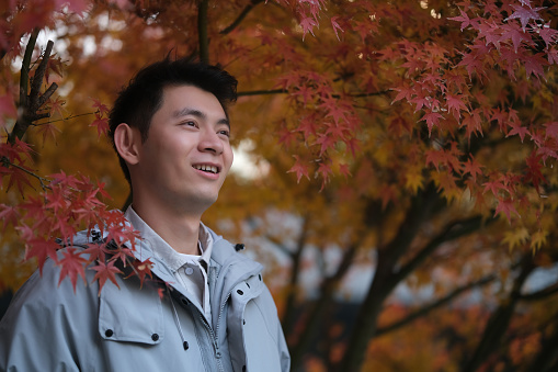 smile handsome Asian Chinese young man under red maple tree in autumn