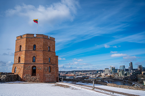 Lithuanian Flag waving on a Gediminas' Castle Tower against the Blue Sky. City centre and River beautiful view in Winter. Vilnius, Lithuania - March 9, 2023.