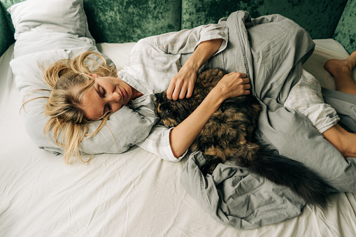 Woman spending morning with her cat lying in bed after waking up.