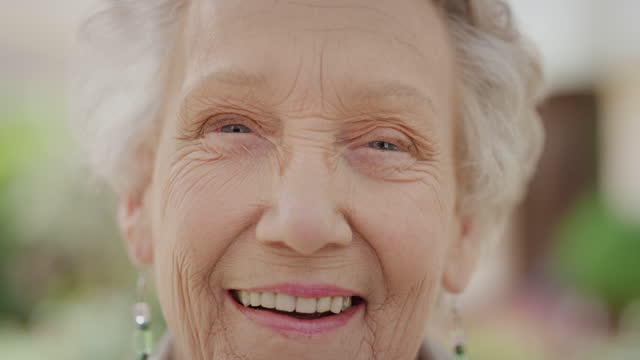 close up portrait of elderly caucasian woman laughing cheerful looking at camera enjoying happy retired lifestyle in sunny outdoors slow motion wrinkled skin