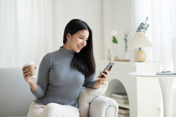 istock Young attractive Asian female using smartphone while sitting on the sofa in living room. 1490358119