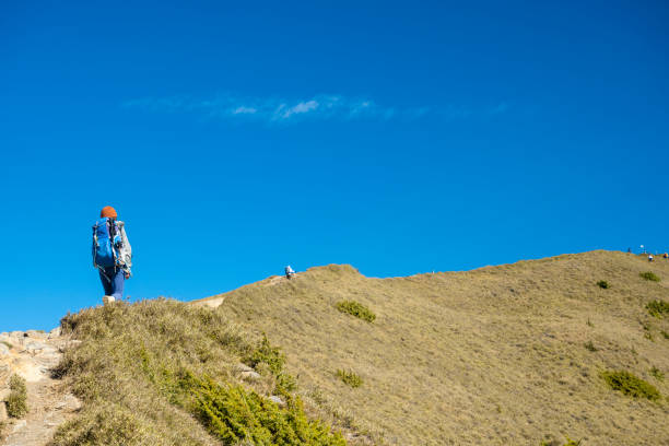 Silhouette of a man walking on a meadow on a hill. Sun and sky in the background.