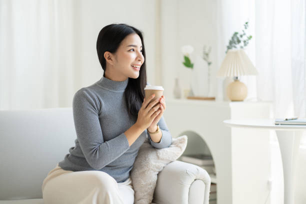 istock Young Asian woman drinking coffee while sitting at her couch. 1490360590