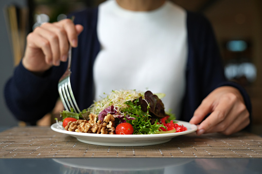 Cropped image of woman having healthy green salad with alfalfa sprouts, cherry tomatoes, walnuts, leafy vegetables, olives, and salad dressing.