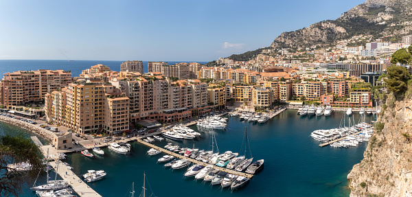 National flag, modern residential buildings and luxury yachts in Port Hercule under blue sky in Monte Carlo, Monaco.