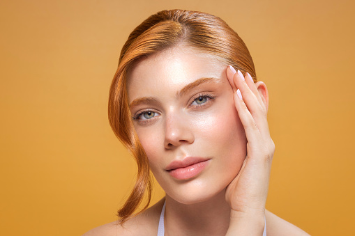 Studio shot of a beautiful redhead woman with perfect skin, applying facial serum on skin.