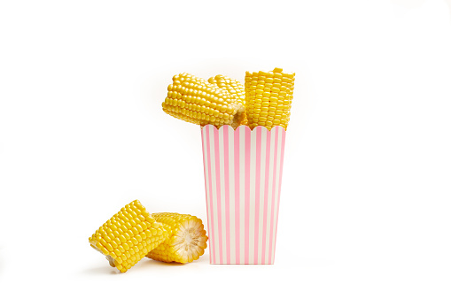 Pieces of corn in a pink and white striped bucket and on a white background with copy space