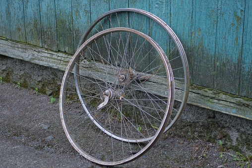 two gray metal bicycle wheels stand against a green wooden wall in the street