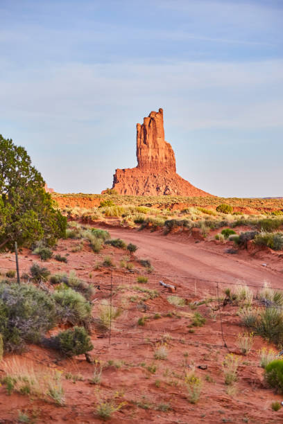 大きな赤い岩柱の隣の砂漠の未舗装の道路とフェンス - usa dirt road rock sandstone ストックフォトと画像