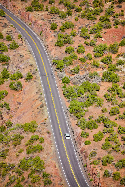 istock Down view of road curving through open desert with white car 1490381907