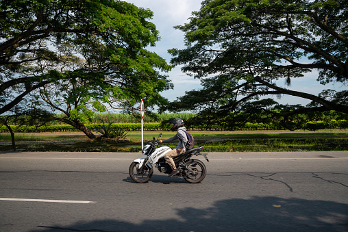 Motorcyclist on a highway with leafy trees in Valle del Cauca. South America. Colombia. July 7, 2022.