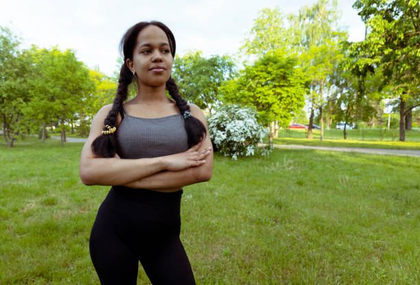 A young African-American woman in a gray tank top stands in a park