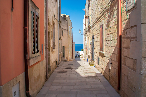 Narrow street located at the top of the hill from which the Ionian Sea can be seen in the background.