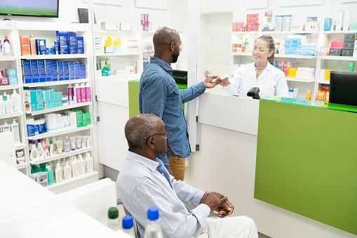 Son helping senior father on wheelchair at the pharmacy