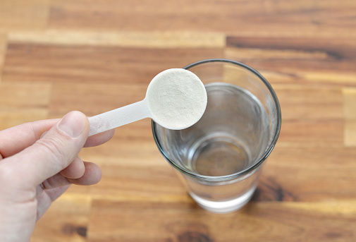 Closeup of a man's hand holding a scoop of protein powder on top of a glass of water.