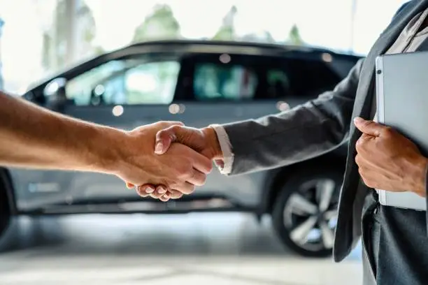 Buyer of the car shaking hands with the seller in the auto dealership. Close-up of handshake of business people.
