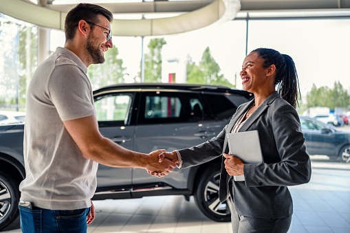 Buyer of the car shaking hands with the seller in the auto dealership.