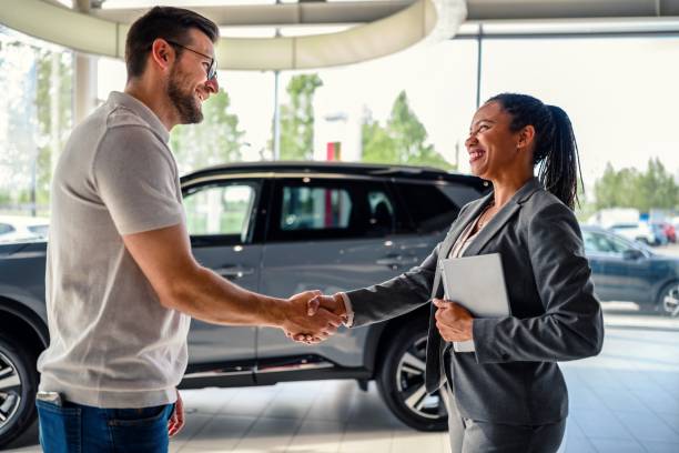 Buyer of the car shaking hands with the seller in auto dealership stock photo