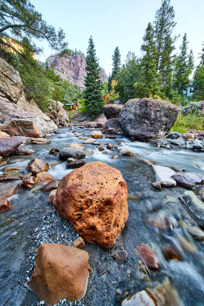 Image of Large red rock in clear shallow riverbed with mountain in distance