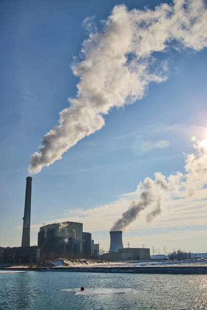 Image of Manufacturing facility on water with two large silos releasing smog into air