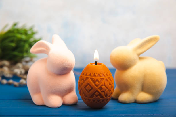 Easter candle eggs in a nest, an Easter bunny and willow branches on a blue table and a blurred light background. Easter holiday concept.Spring willow bouquet.Decor for home and festive steel.