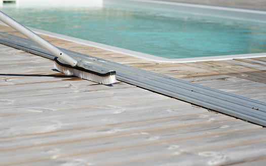 Cleaning brush on the wooden deck next to the outdoor swimming pool on a sunny summer day. Photo taken in Sweden.