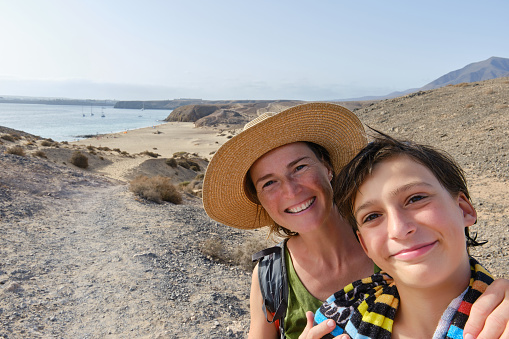 Mother and son taking a selfie at the beach with smartphone. Mature woman and preteen boy enjoying time together.