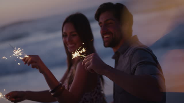 happy young couple waving sparklers dancing celebrating new years eve on calm beach sunset background sparkle firework