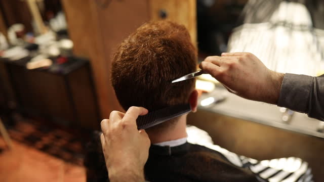 Barber using scissors and comb while cutting customer's hair in barbershop