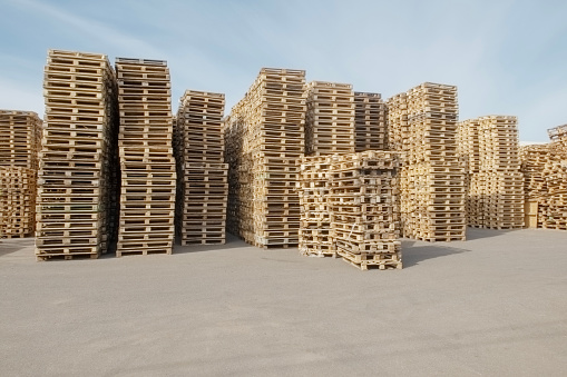 high stacks of pallets stacked on top of each other in an open-air warehouse