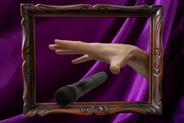 Photo of Caucasian male's hand dropping the mic, stretched hand and a microphone coming out of a levitating wooden frame