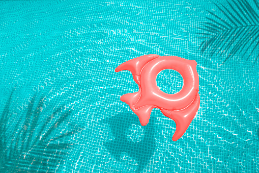 Swimming pink inflatable ring floating in a refreshing green swimming pool with palm tree leaf shadows in the water. Web banner, template, summer background