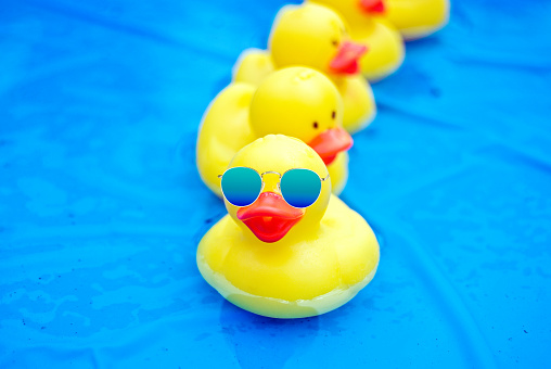 Yellow rubber duck wearing blue gradient sunglasses in blue wading pool