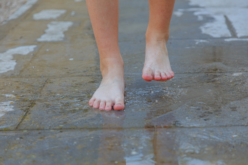 Child legs and feet walking in puddle water with mud barefoot during summer day