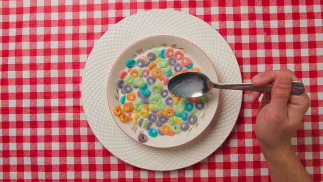 Top view of the hands of a lonely man eating colorful cereal for breakfast, lack of appetite.