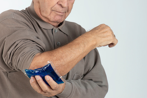 Elderly man holding an ice pack for elbow pain.