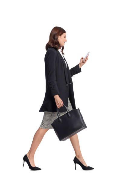 istock Happy young woman in formal suit using smartphone while walking on white background 1490423492