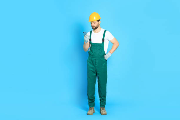 istock Professional repairman in uniform with smartphone on light blue background 1490425058