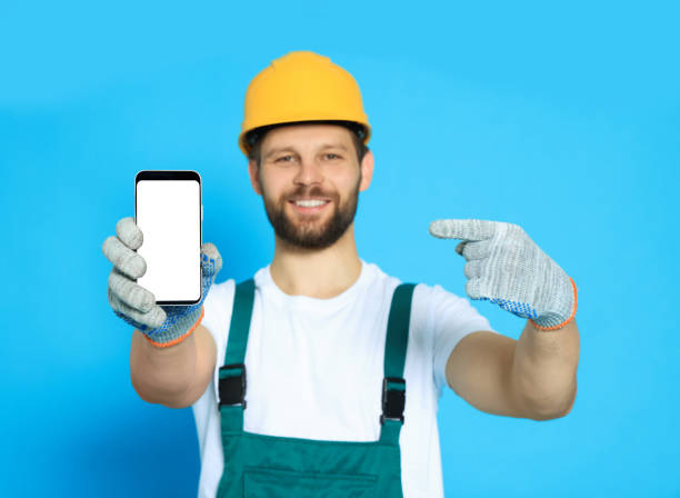 istock Professional repairman in uniform showing smartphone against light blue background, focus on screen 1490425094